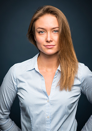 Porträttfoto i studio på Alexandra Lindström klädd i ljusblå skjorta med blicken mot kameran.