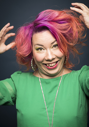 Porträttfoto i studio på sprallig Emelie Klintecorn med rosaorange hår och båda händerna i luften.