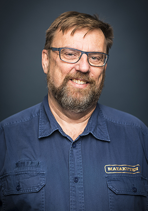Porträttfoto i studio på Lasse Wennman i en blå skjorta leendes mot kameran.