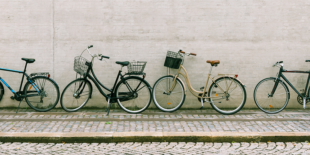 Fyra cyklar står lutade mot en husvägg.