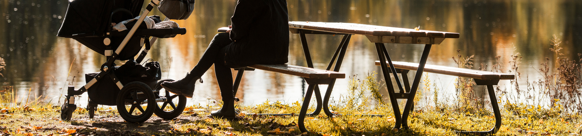 EN kvinna som sitter på en bänk och har en barnvagn till vänster om sig