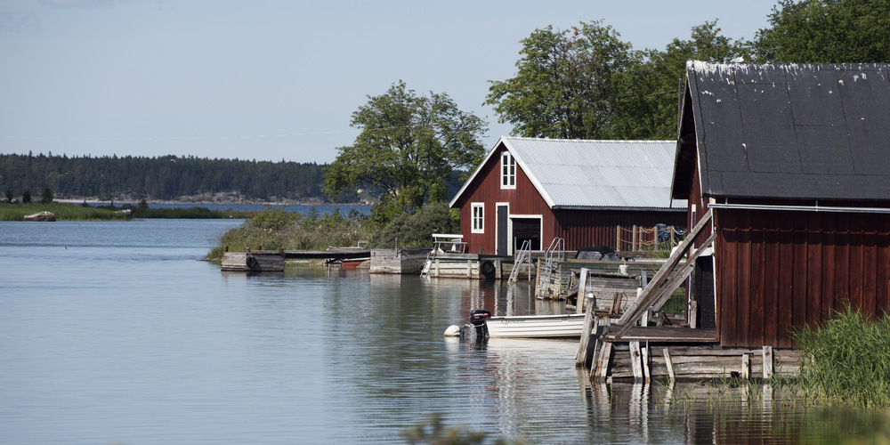 Två båthus vid vattnet. En liten eka ligger vid en brygga intill