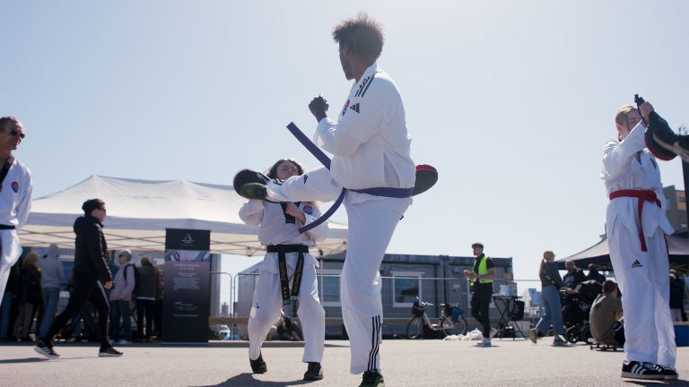 Personer som utför taekwondo utomhus på asfalt.