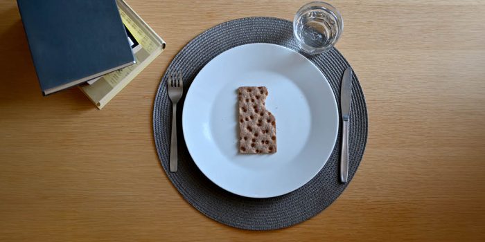 Bord med knäckebröd på vit tallrik, bestick, glas och böcker.