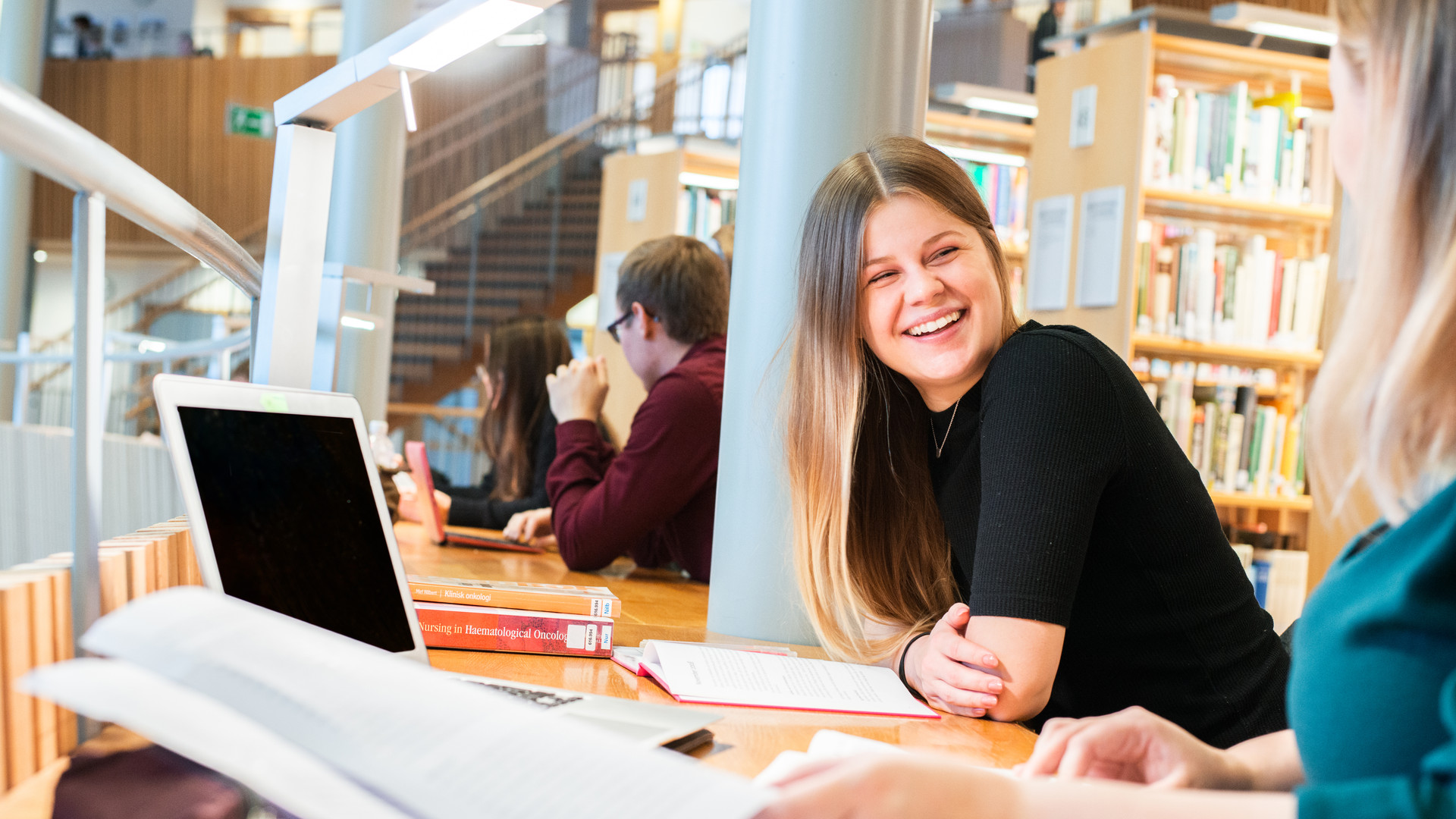 En person som sitter i ett bibliotek med en dator framför sig.