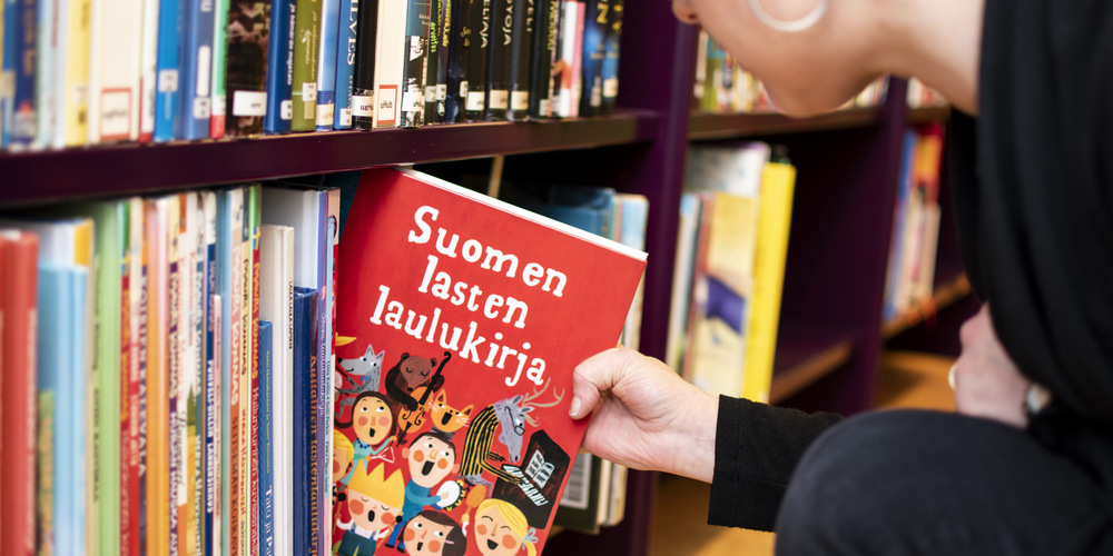 En bok i fokus. En person tar en bok från en bokhylla