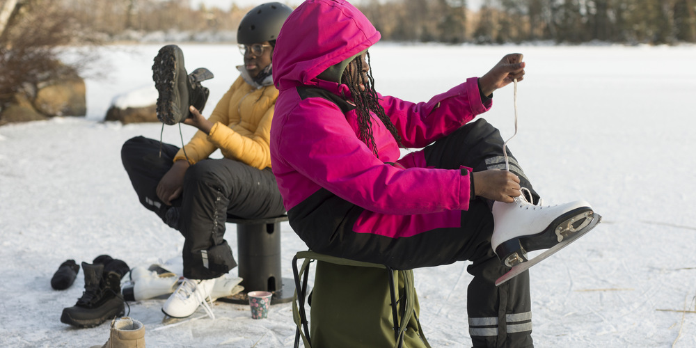 Två personer som sitter och knyter på sig skridskor.