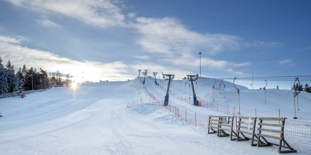 En skidbacke med snö i. Himlen är blå och till höger syns en knapplift.