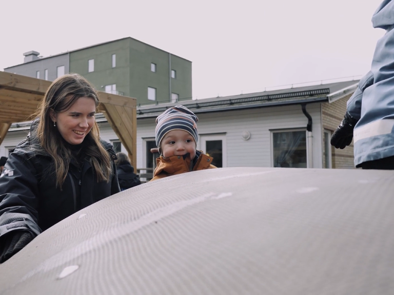 En fritidspedagog står med barn som åker rutschbana